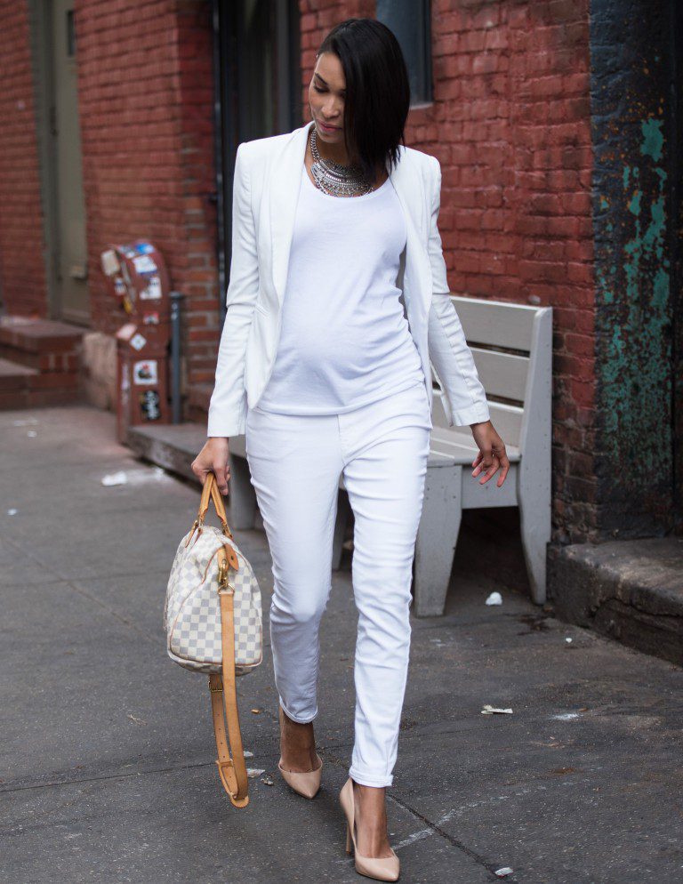 Woman in white suit walking, carrying handbag.