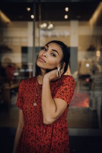 Woman in red floral dress, hand on neck.