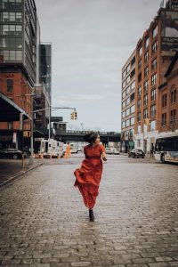 Woman in red dress on cobblestone street.