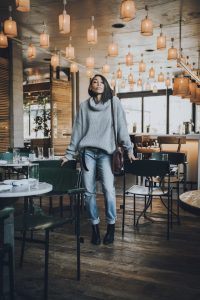 Woman in sweater and jeans in cafe.