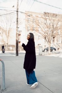 Smiling woman in black coat, jeans.