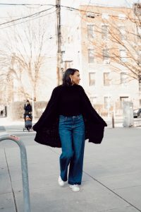 Woman in black cardigan and jeans walking.