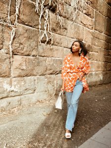 Woman in floral dress walking by stone wall.