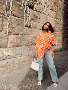 Woman in floral top, jeans, and white shoes.