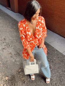 Woman in floral dress, jeans, and white bag.