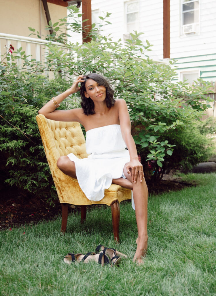 Woman in white dress sits outdoors.