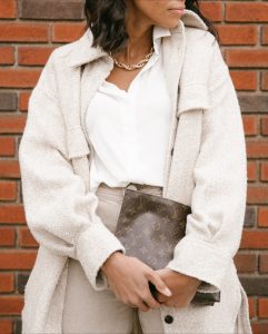 Woman in beige coat holding Louis Vuitton bag.