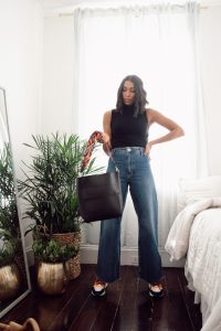 Woman in jeans holding black tote bag.