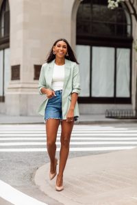 Woman in green blazer and denim shorts.